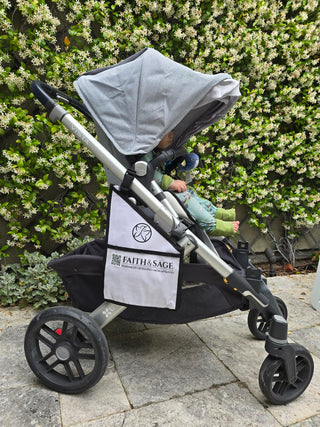Stroller with a child inside, branded 'Faith & Sage', against a green bush background.