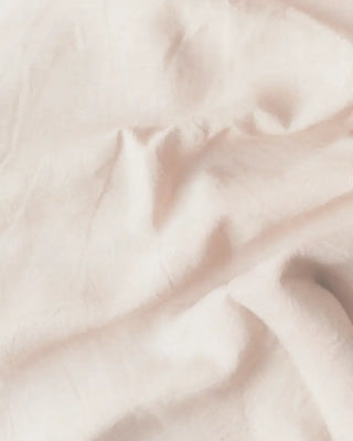 A close-up of softly draped pale blush pink fabric with a smooth, slightly sheer texture.